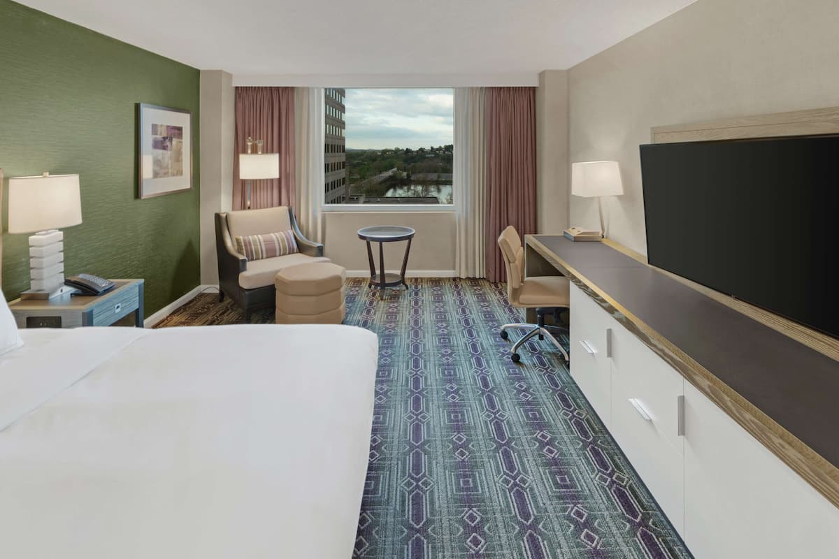A hotel room with a bed, a desk, a chair, a small table, and a TV.