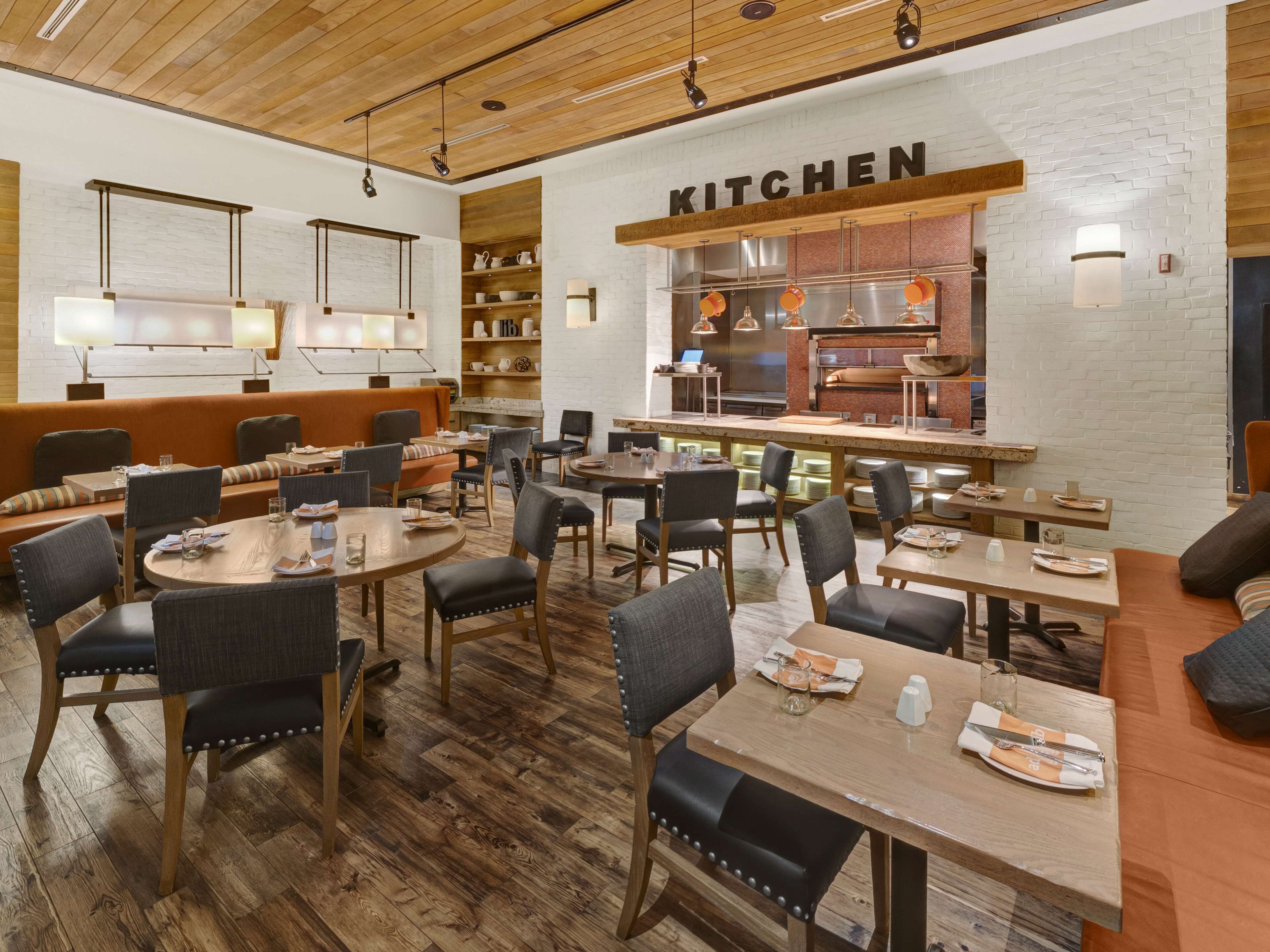 Restaurante com área de cozinha, piso de madeira e disposição de mesas e cadeiras.
