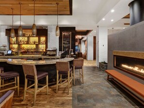 A bar area with a counter, stools, and a fireplace. - Hilton Harrisburg (Harrisburg)