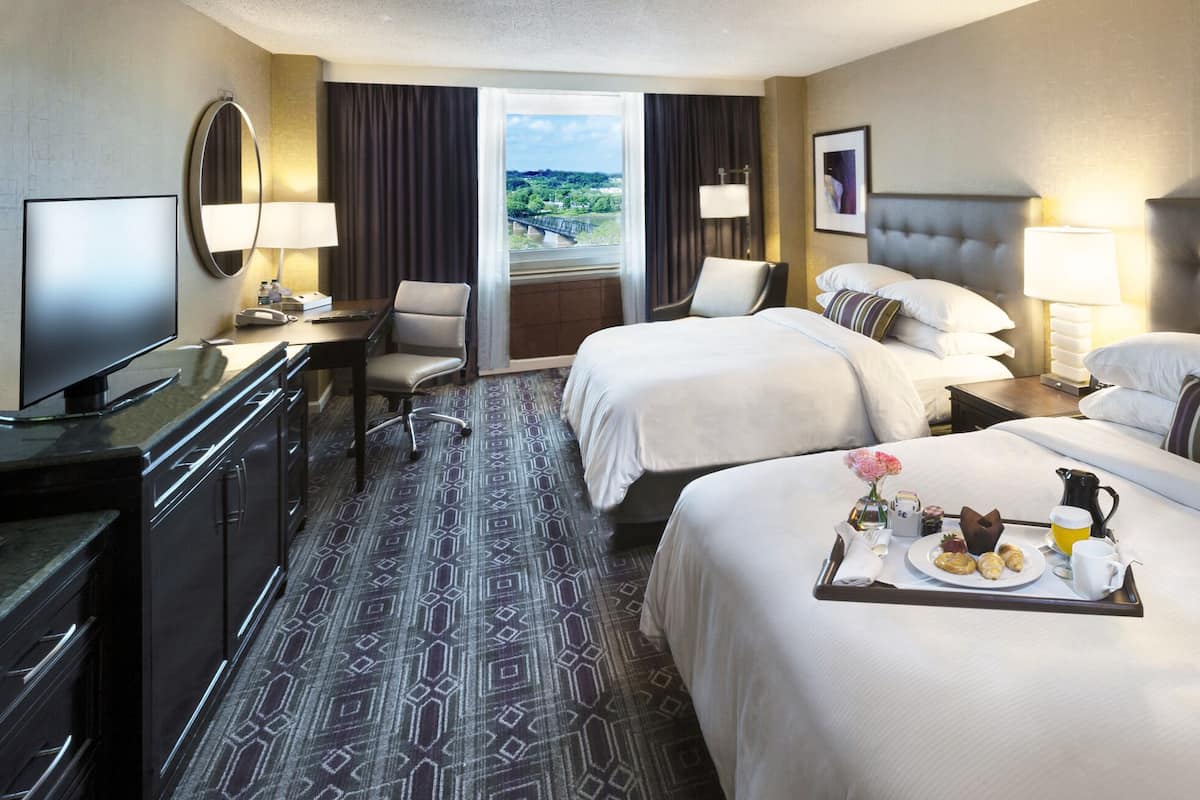 A hotel room with two beds, a desk with a TV, a chair, and a dining table with breakfast.