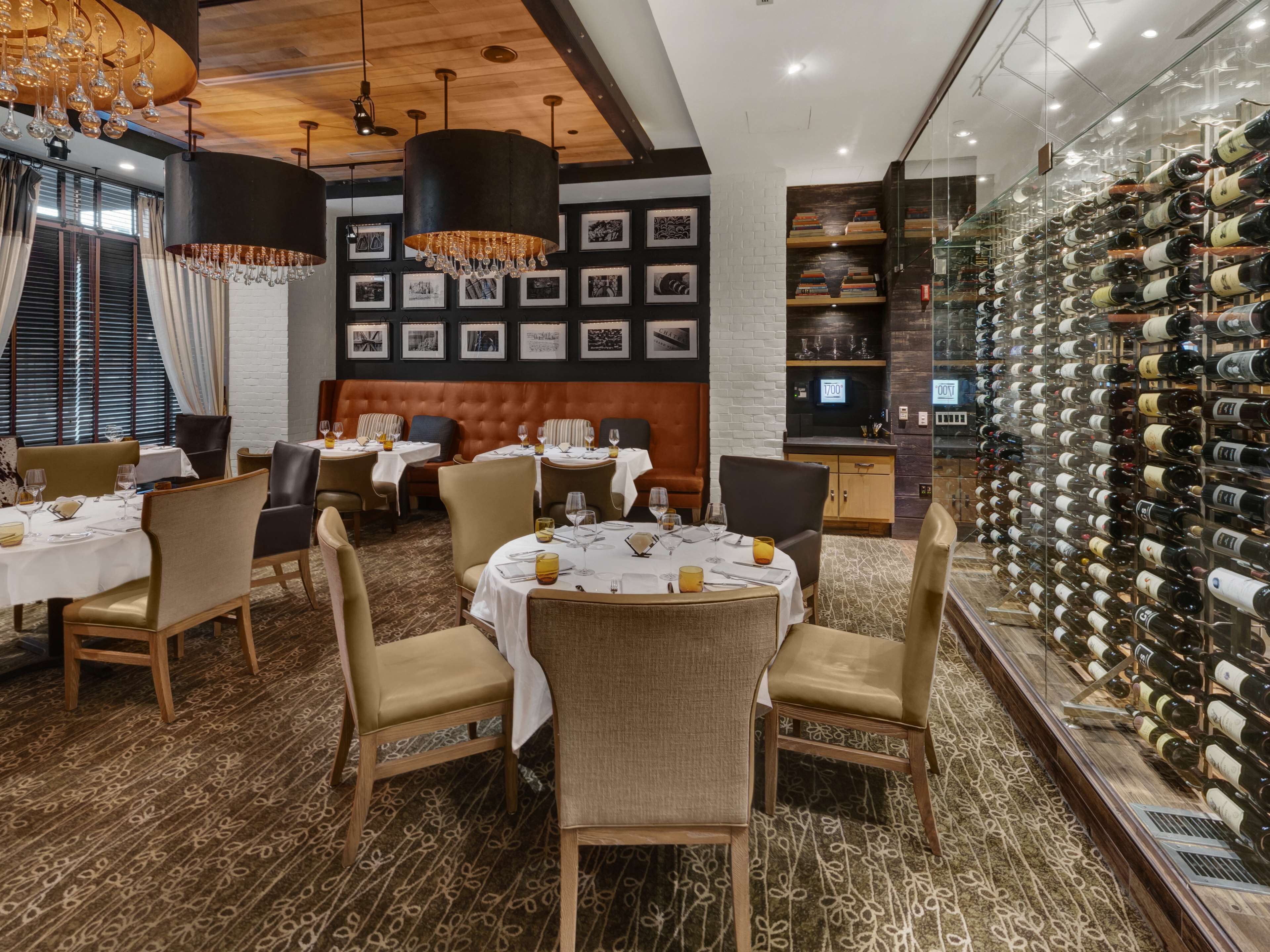 Een restaurant met ronde tafels, stoelen en een wijnwand.