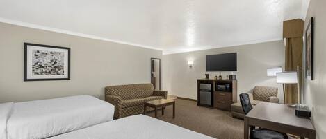 A hotel room with two beds, a desk, a chair, a sofa, a TV, and a minibar.