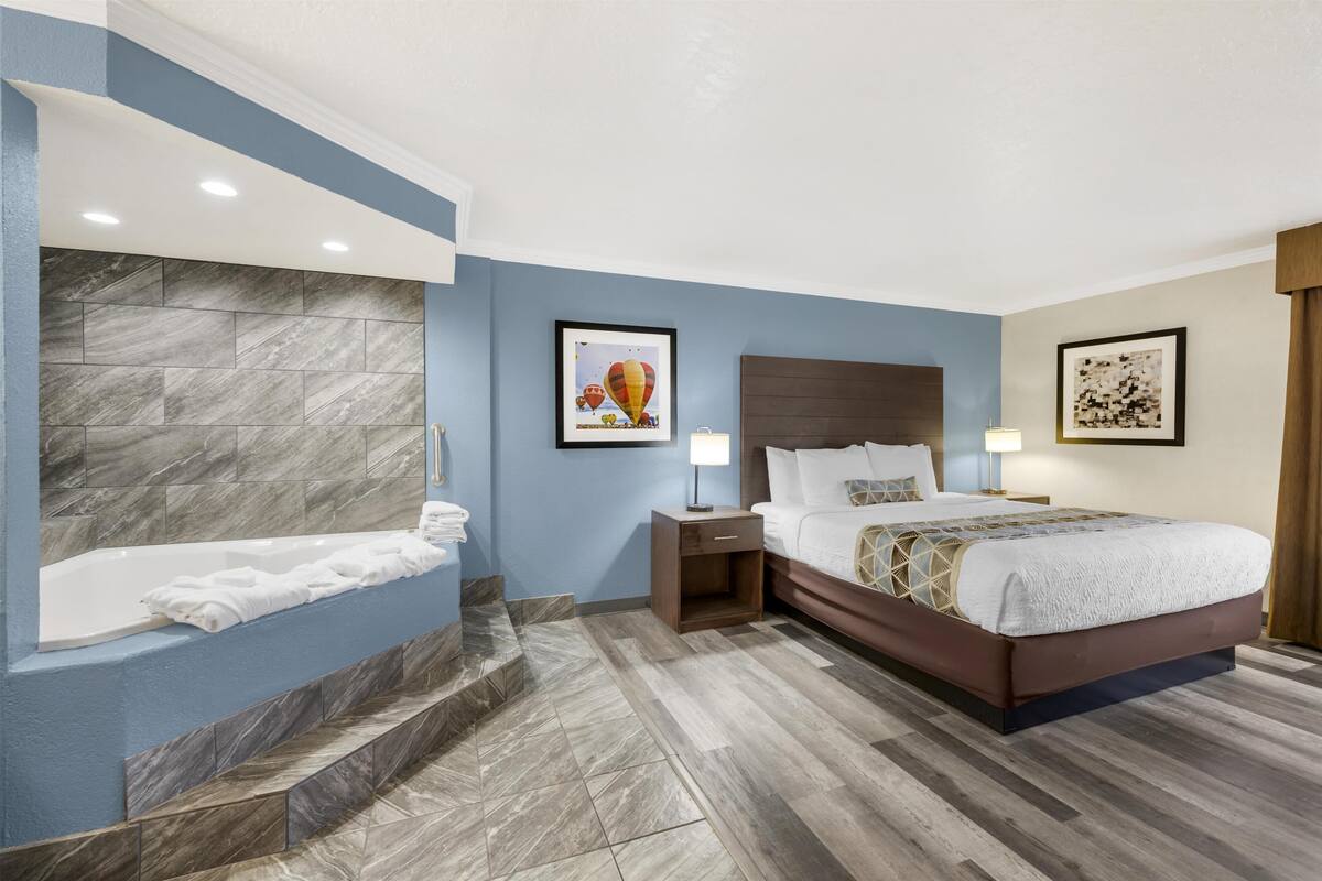 Een moderne hotelkamer met een marmeren wand, een groot bed met een sprei met geometrisch patroon, een nachtkastje met lamp en een lijst met een afbeelding van luchtballonnen.