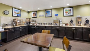 A hotel kitchen with a wooden table and chairs, a clock, and framed artwork on the walls. - Best Western Airport Albuquerque InnSuites Hotel & Suites (Albuquerque)