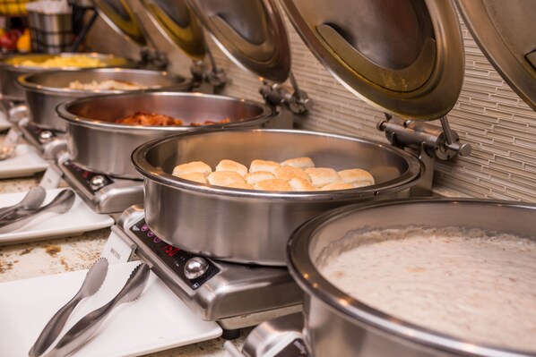 Disposición de bufé con diferentes alimentos en recipientes metálicos, incluyendo una olla grande de arroz y varias ollas más pequeñas con distintos platos.