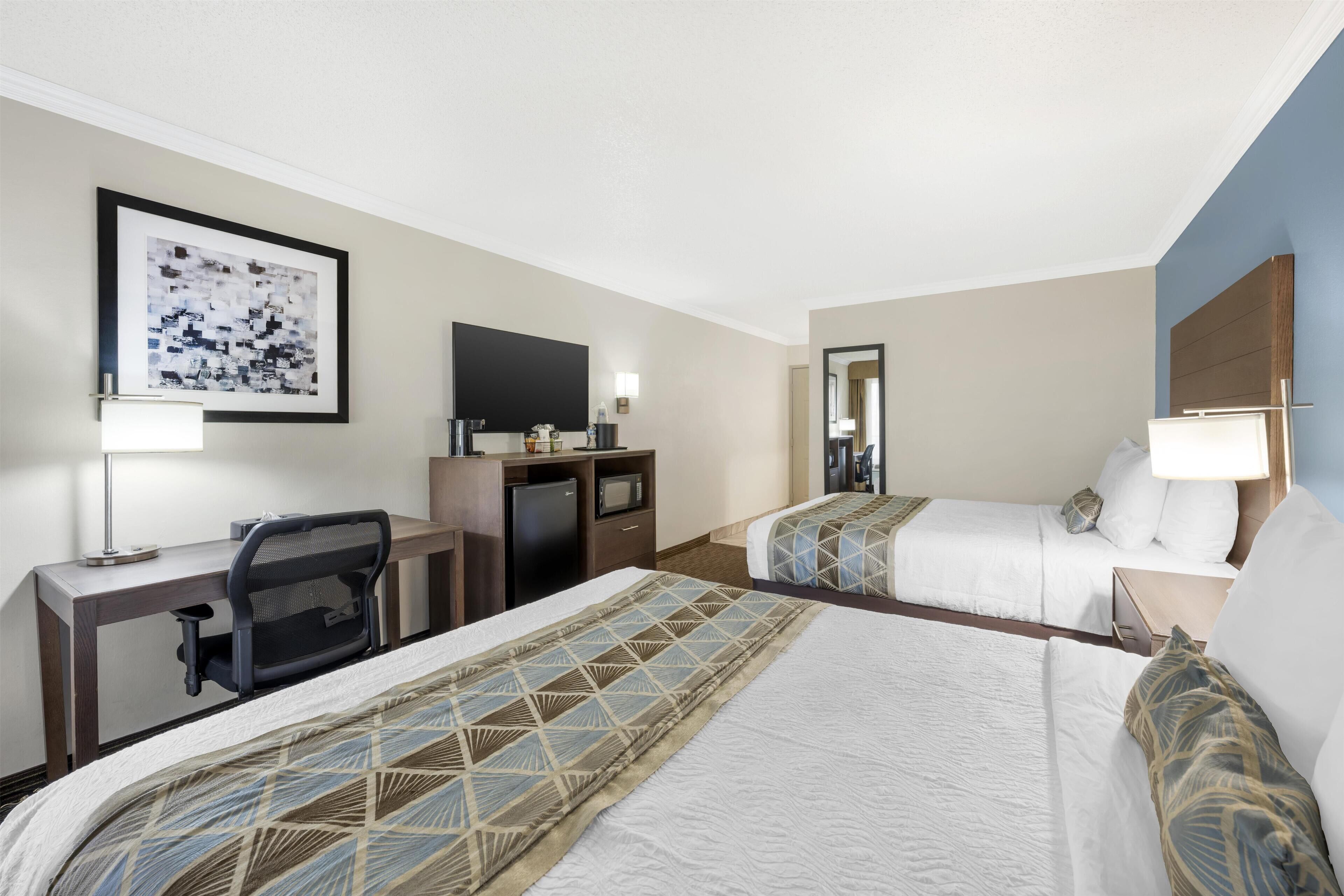 A hotel room with two beds, a desk, a chair, a TV, and a framed picture on the wall.