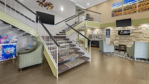 A spacious lobby with a staircase, a seating area, and a stone wall with artwork. - Best Western Airport Albuquerque InnSuites Hotel & Suites (Albuquerque)