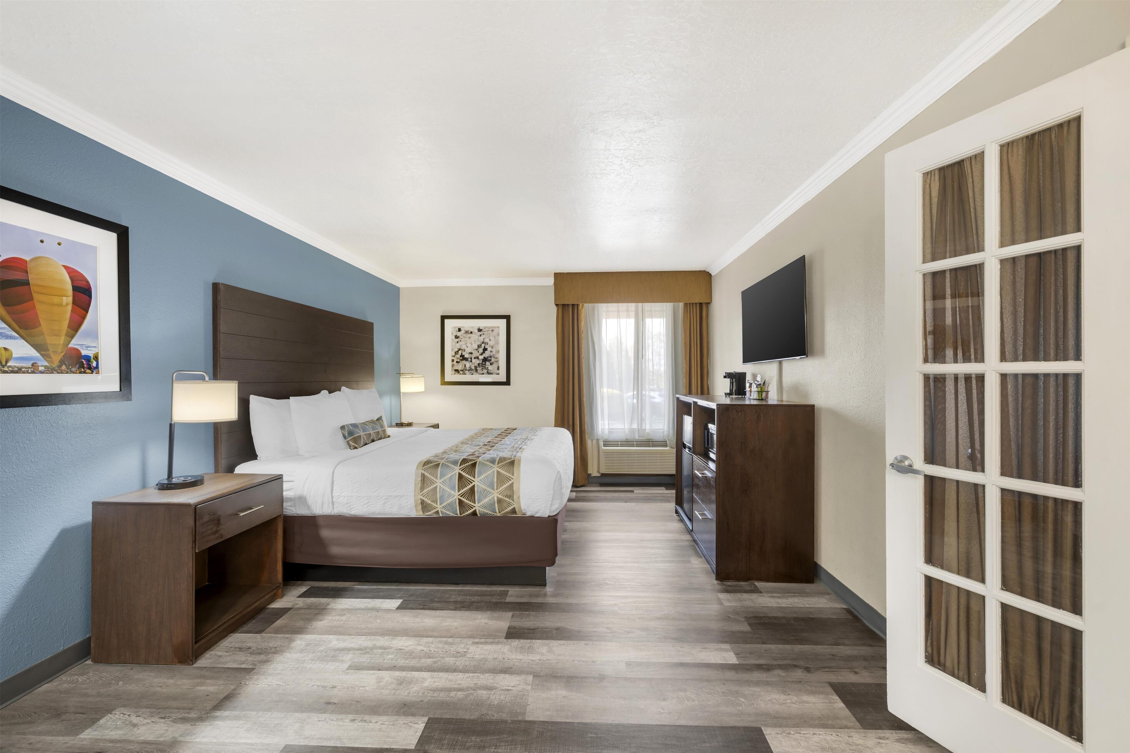 A hotel room with a bed, bedside table, lamp, artwork, and a television.