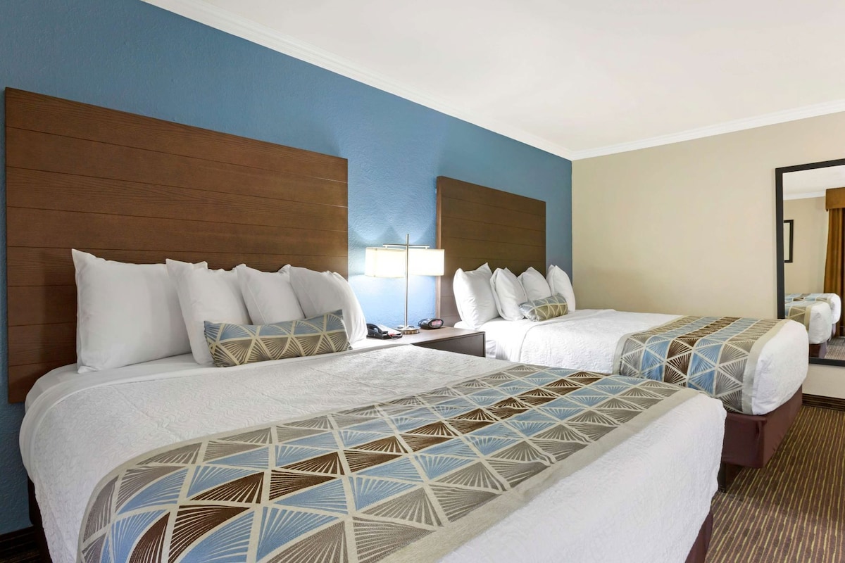 A hotel room with two beds, a nightstand, a lamp, and a mirror.
