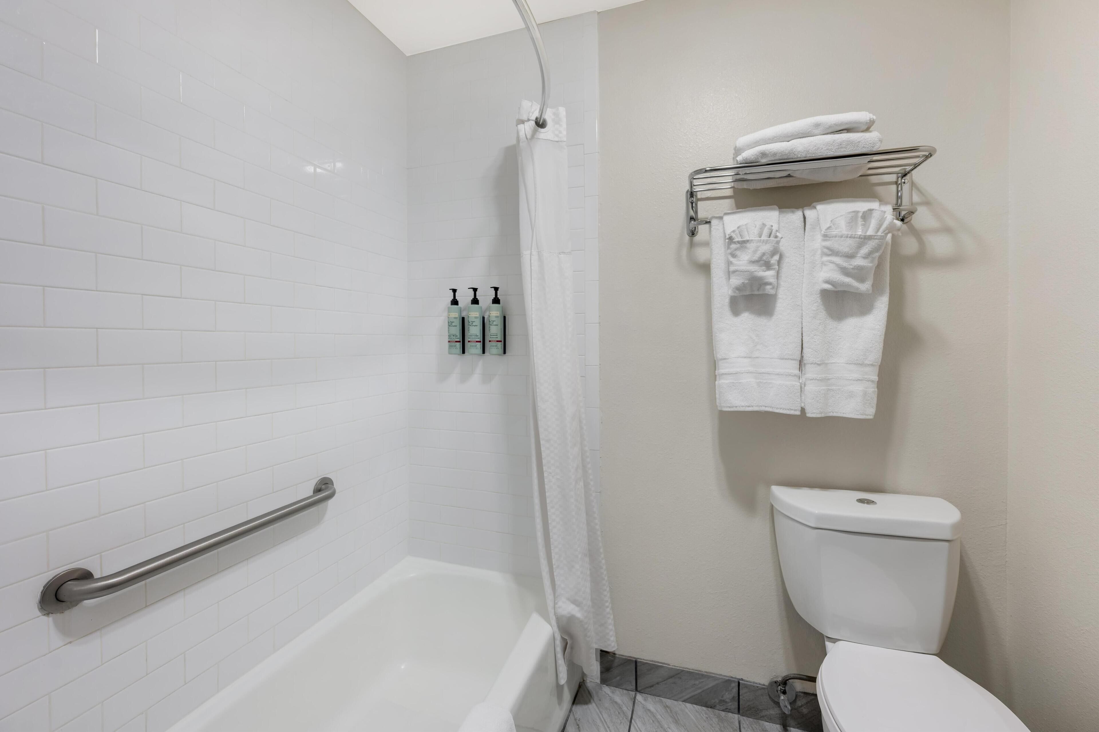 A bathroom with a white bathtub, a shower curtain, a toilet, and a towel rack with towels.