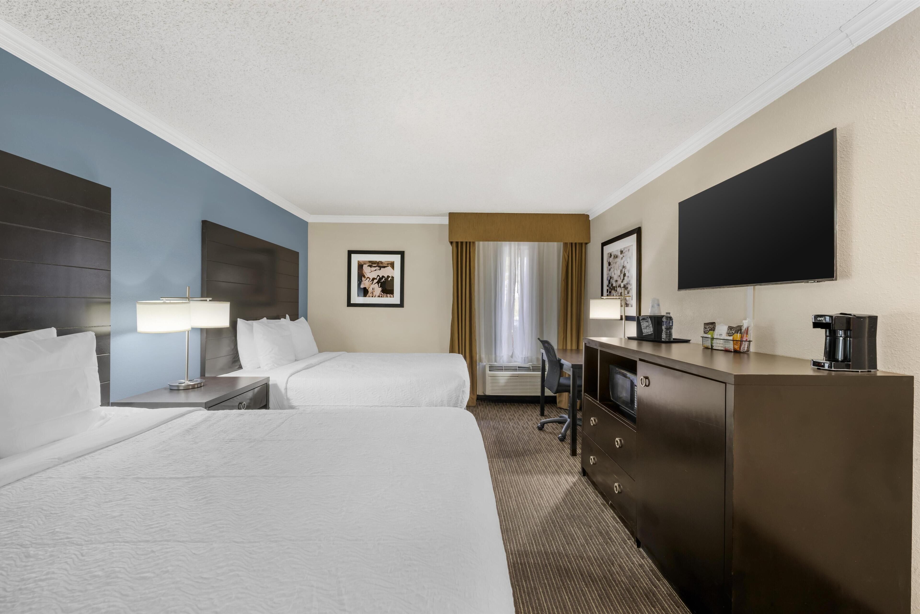 A hotel room with two beds, a desk, a TV, and a coffee machine.