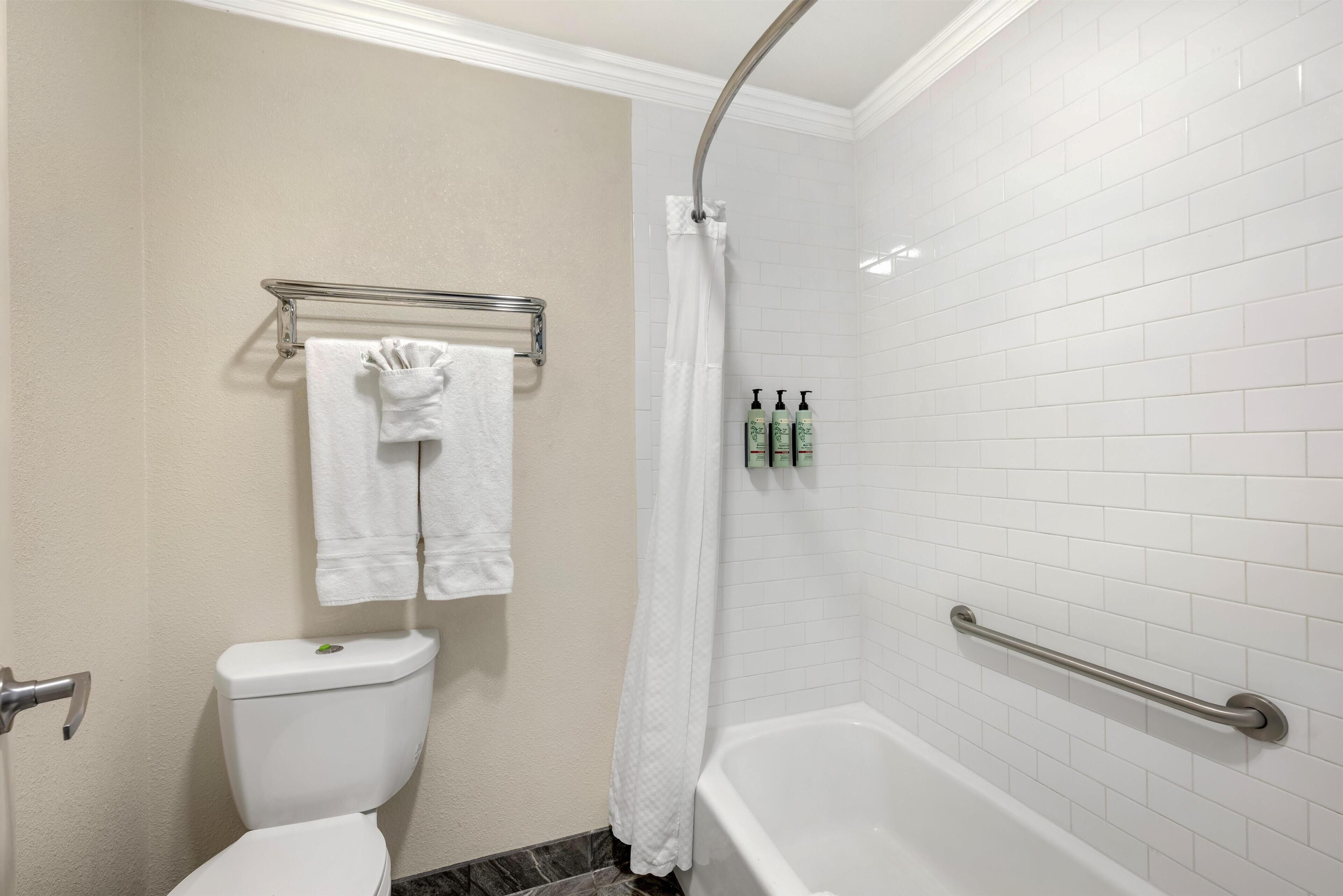 A bathroom with a white bathtub, a shower curtain, a toilet, and a towel rack with two towels.