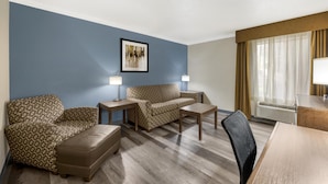 A hotel room with a blue accent wall, a sofa, a loveseat, a coffee table, a chair, and a desk with a lamp. - Best Western Airport Albuquerque InnSuites Hotel & Suites (Albuquerque)