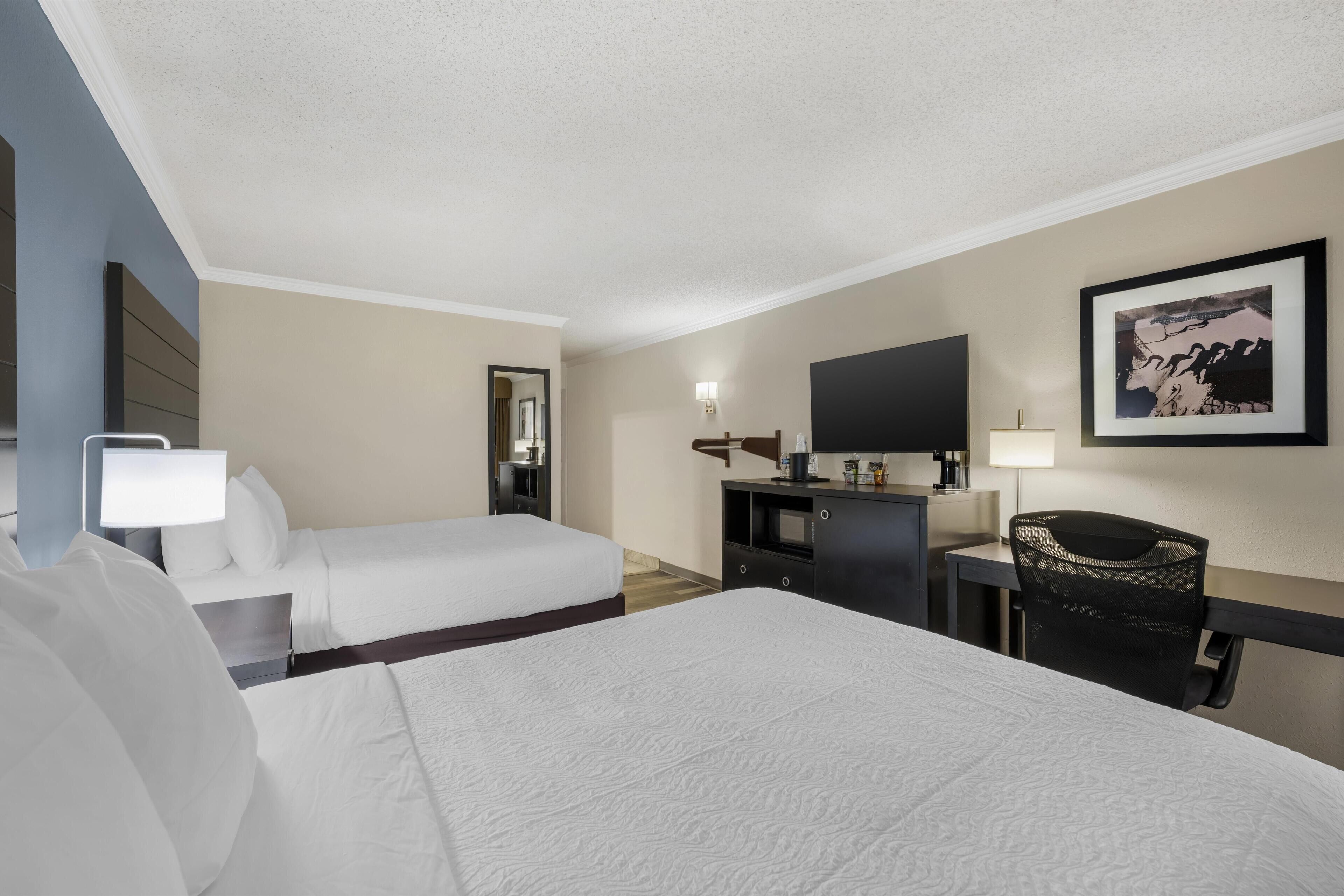A hotel room with two beds, a desk, a chair, a TV, and a framed picture on the wall.