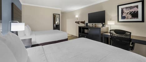 A hotel room with two beds, a desk, a chair, a TV, and a framed picture on the wall.