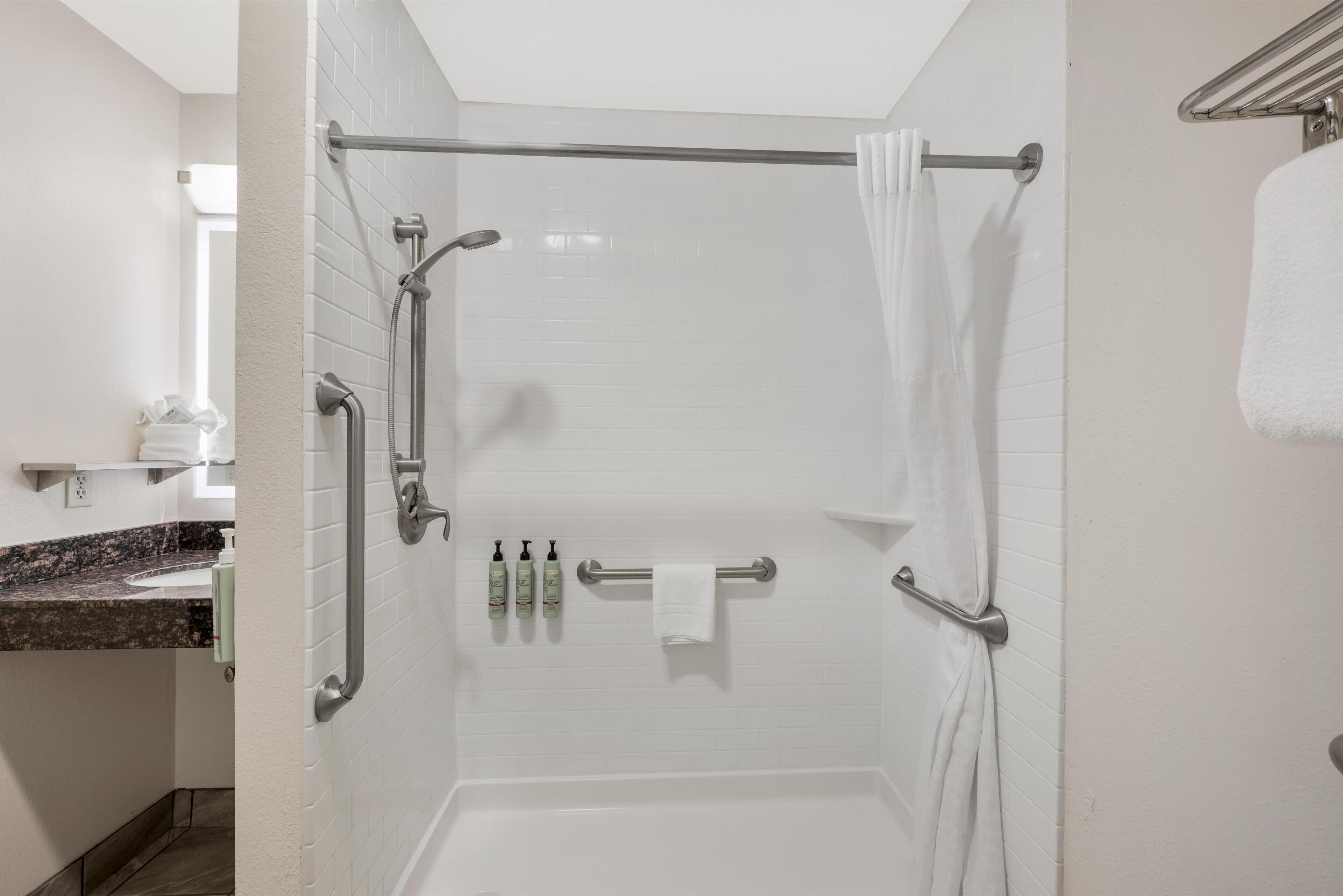 A walk-in shower with a glass door, white tiled walls, a towel rack, and a handrail.