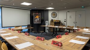 A conference room with a long table, chairs, a projector screen, a clock, and a door with an emergency exit sign. - ibis Nanterre la Défense (Nanterre)
