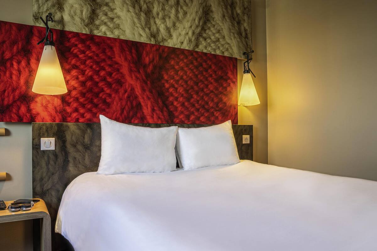 A neatly made bed with white linens, a headboard with a textured design, and two wall-mounted lamps.