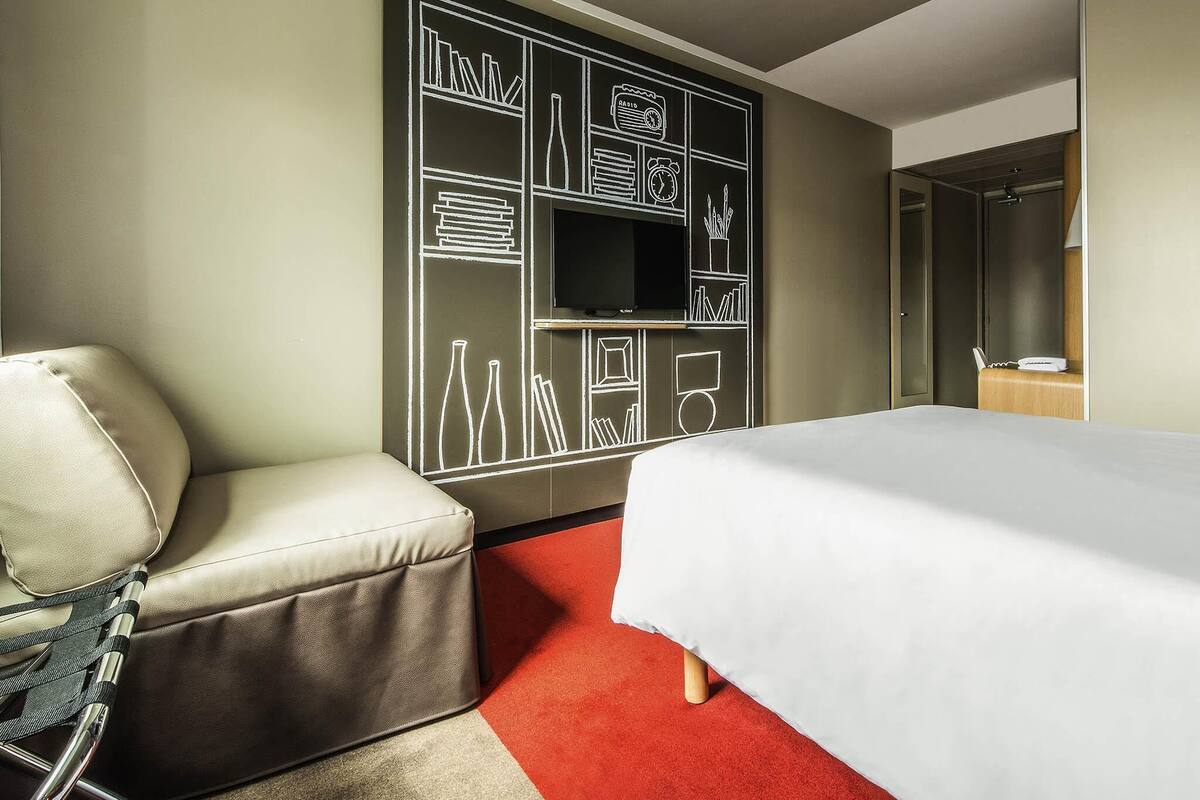 A hotel room with a bed, a seating area, a television, and a mirror.