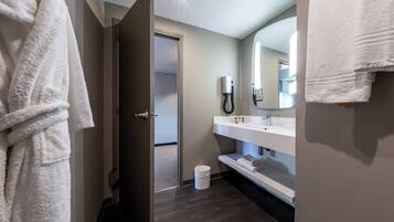 Une salle de bain moderne avec un plancher en bois foncé, un lavabo blanc et un miroir au-dessus.