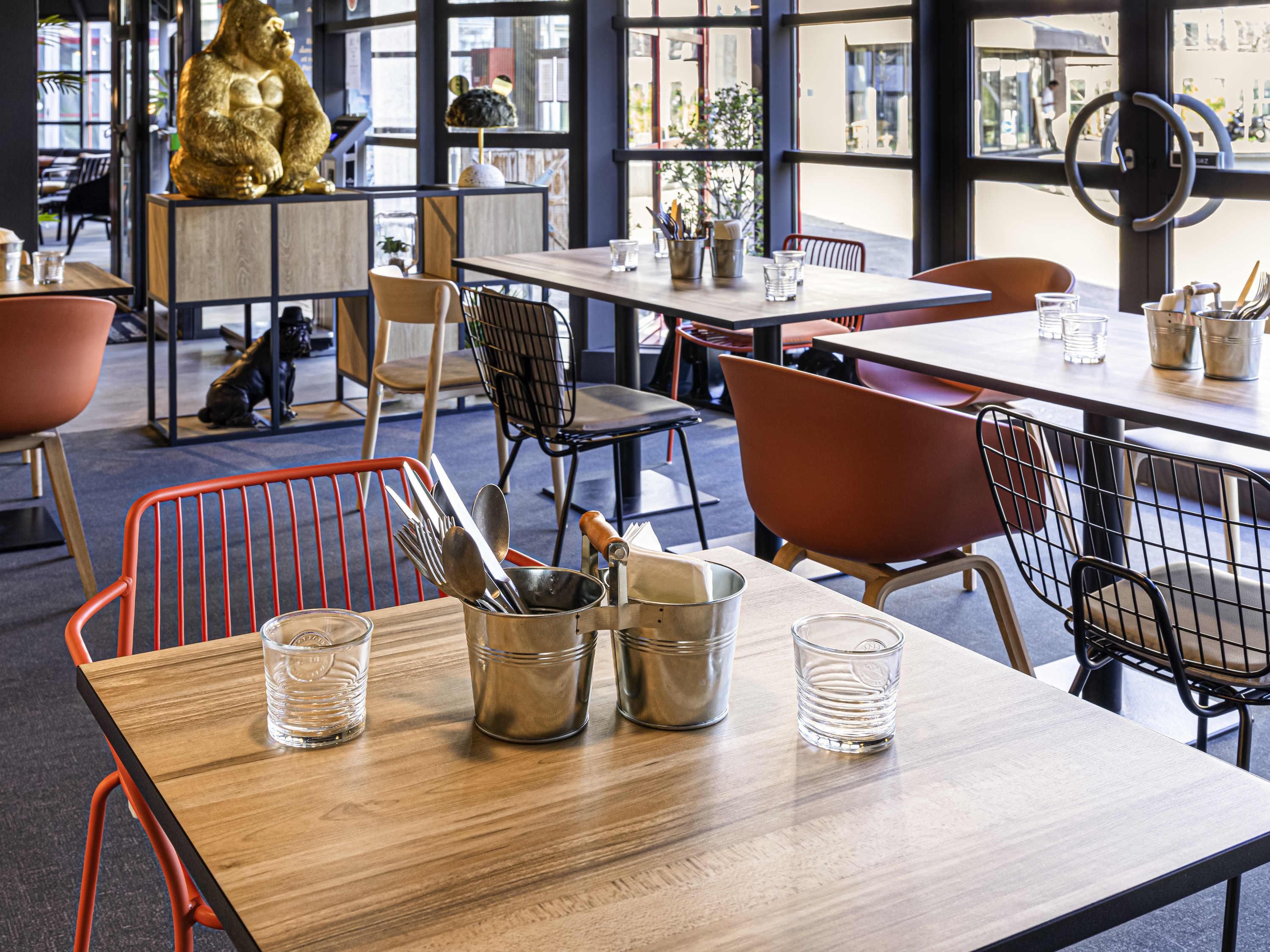 A restaurant interior with wooden tables, metal chairs, and a large window offering a view of the street.