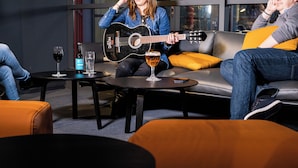 A cozy indoor setting with a person playing a guitar, a table with a bottle and glasses, and a sofa with cushions. - ibis Nanterre la Défense (Nanterre)
