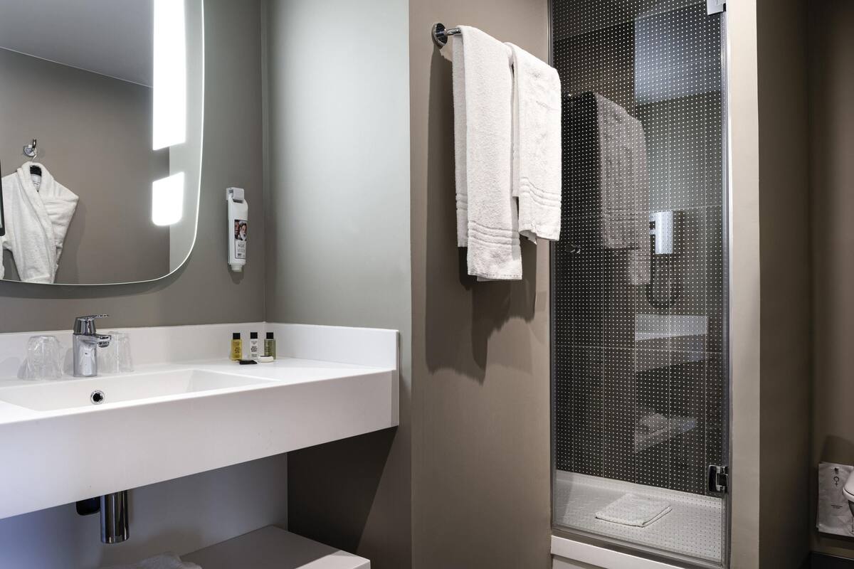 A modern bathroom with a white sink, mirror, and shower area.