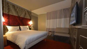 Habitación de hotel con una cama, una silla, un televisor y una pared con diseño decorativo.