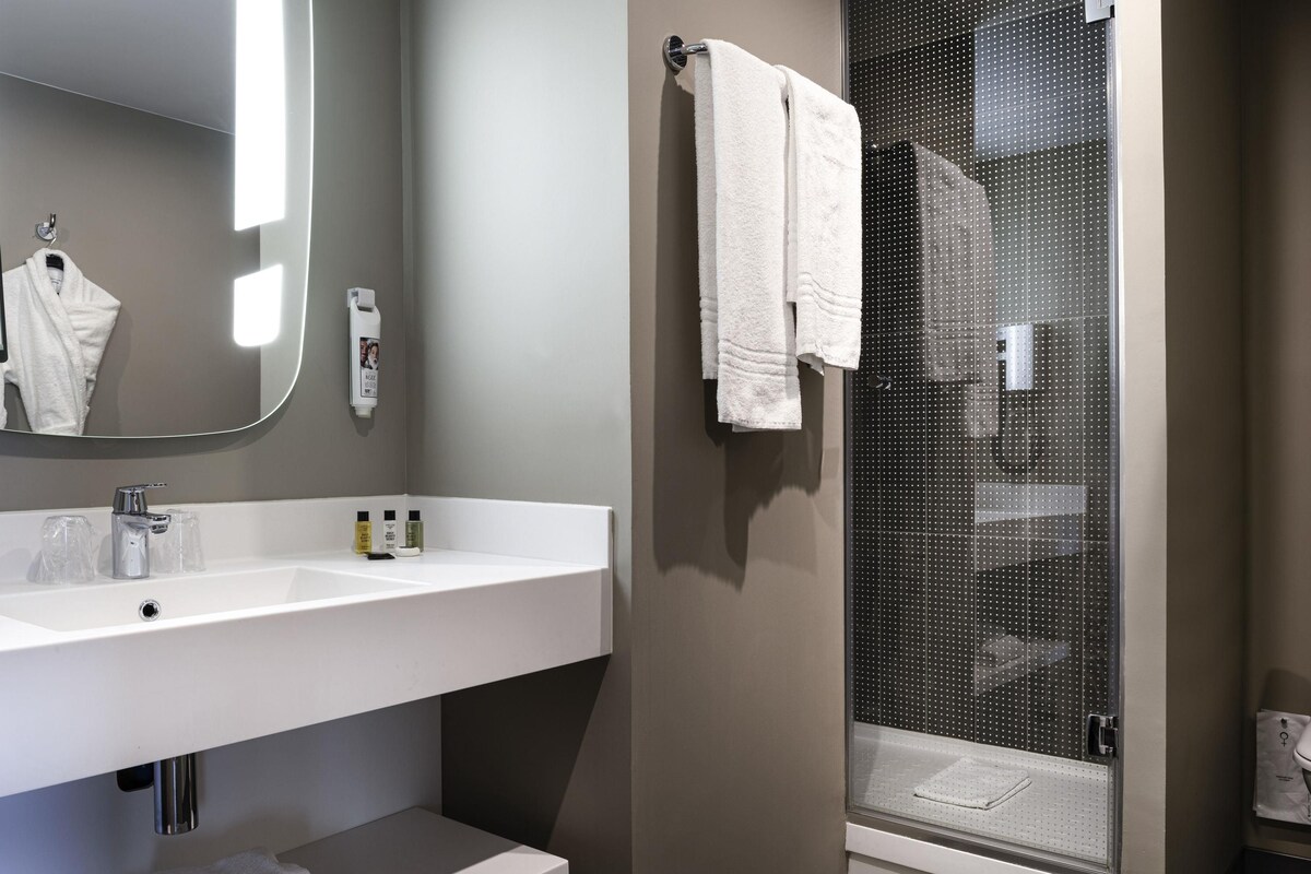 A modern bathroom with a white sink, mirror, and shower area.