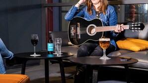 A person playing a guitar in a room with a sofa, a table with a bottle and glasses, and a smartphone on another table. - ibis Nanterre la Défense (Nanterre)