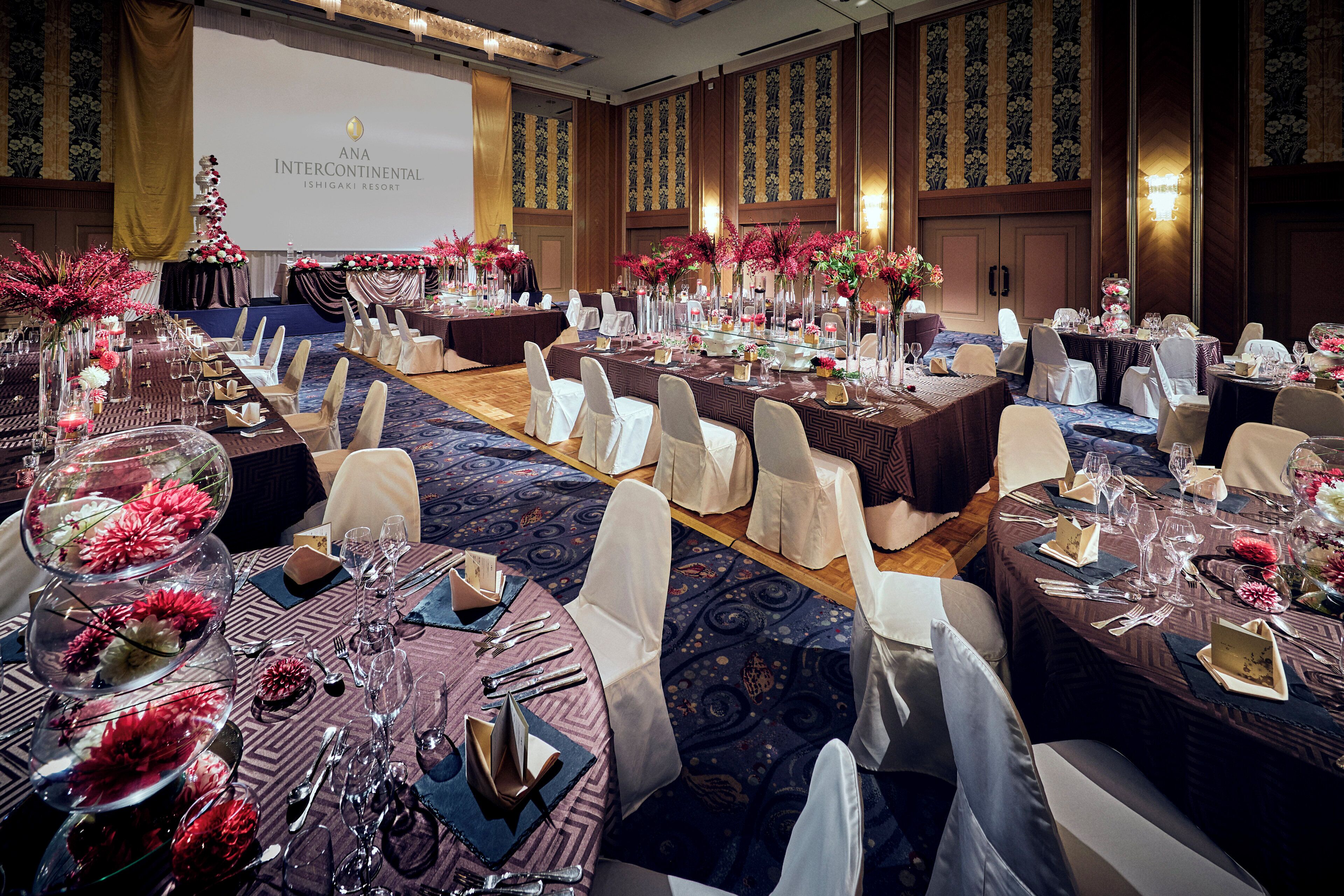 Een feestzaal met ronde tafels, gedekt voor een formeel evenement, met bloemdecoraties en porselein.