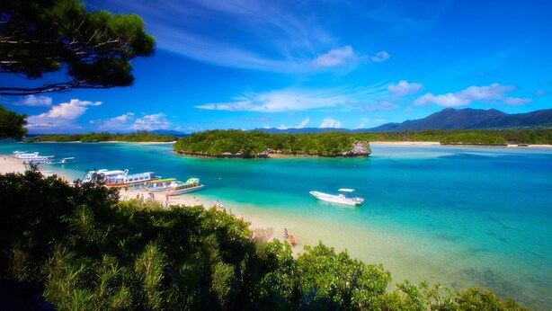 Une plage tropicale avec des bateaux, une eau turquoise cristalline et une végétation luxuriante.