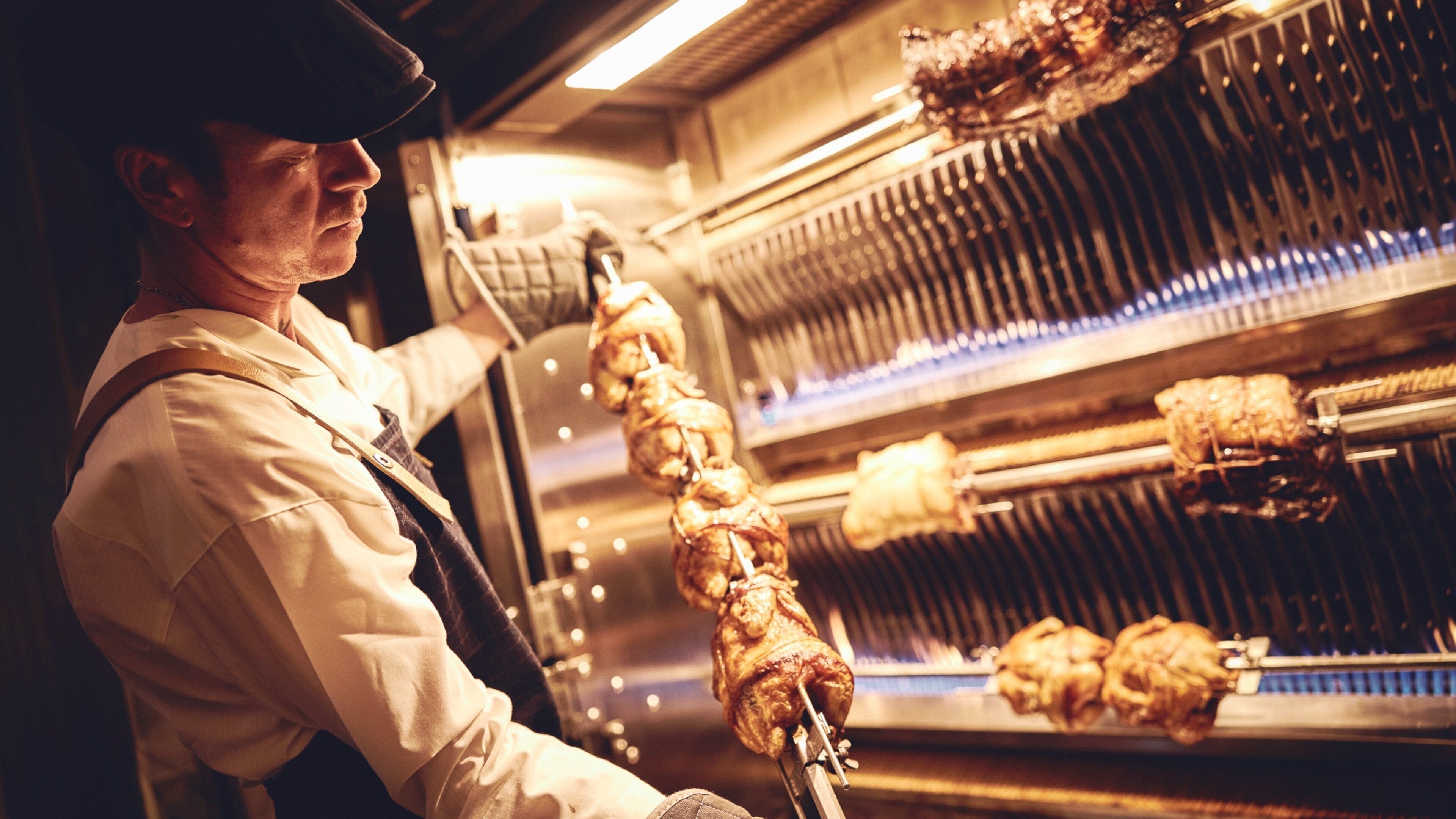 Une personne en uniforme prépare des aliments dans une cuisine équipée d’un grand four industriel.