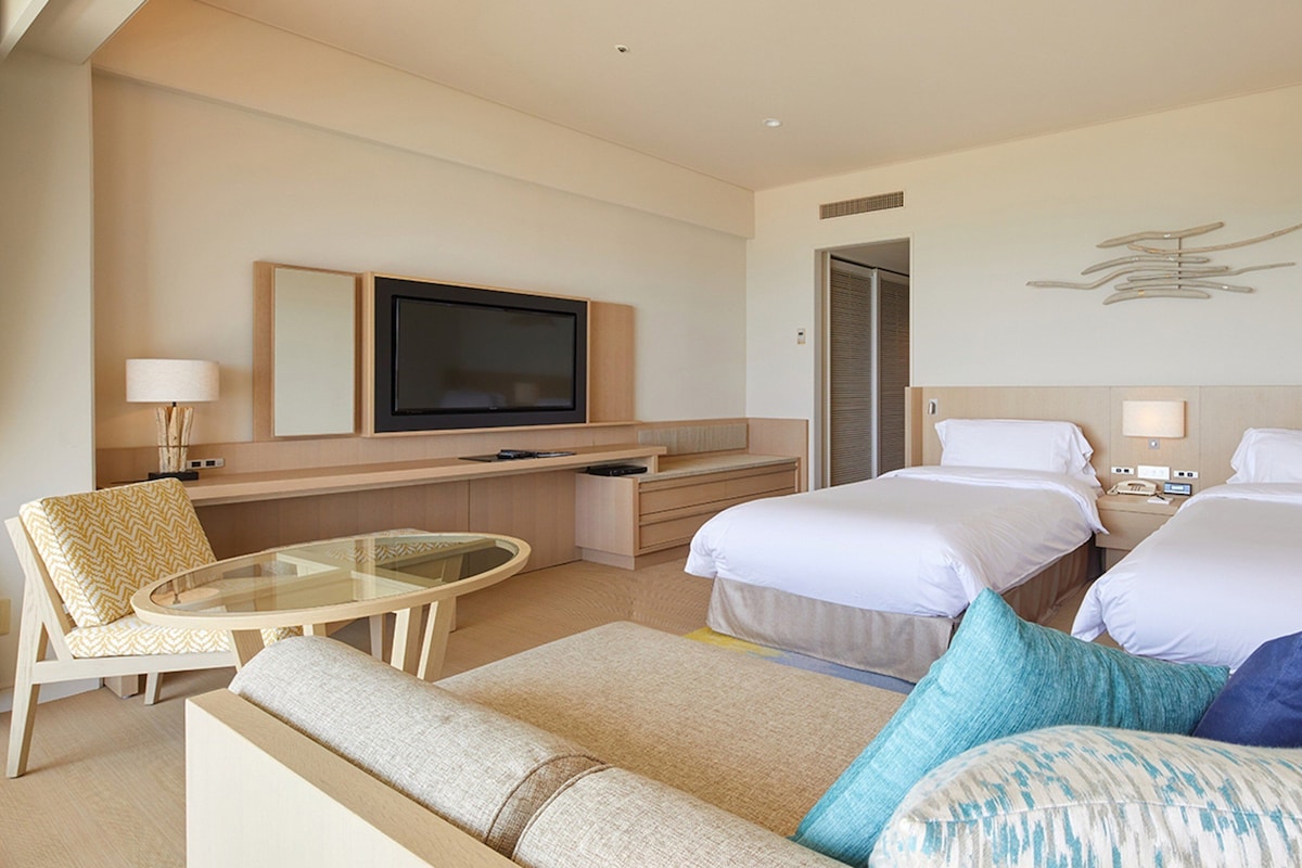 Habitación de hotel con dos camas, televisión, escritorio y zona de estar.