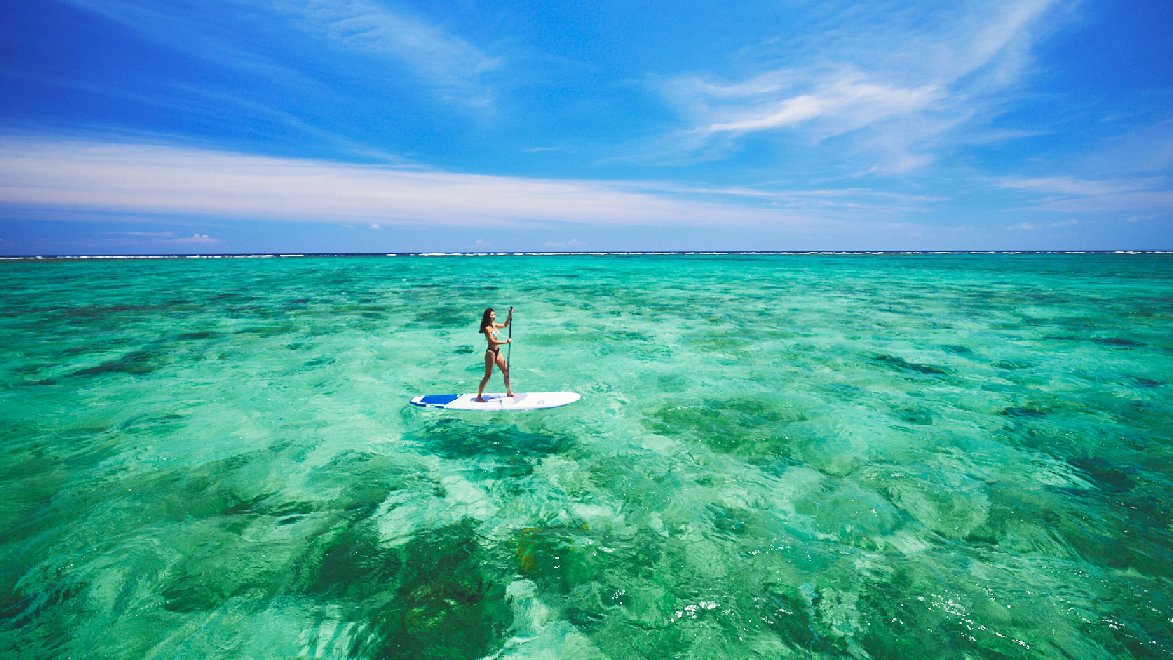 A woman standing on a paddleboard in clear turquoise water.