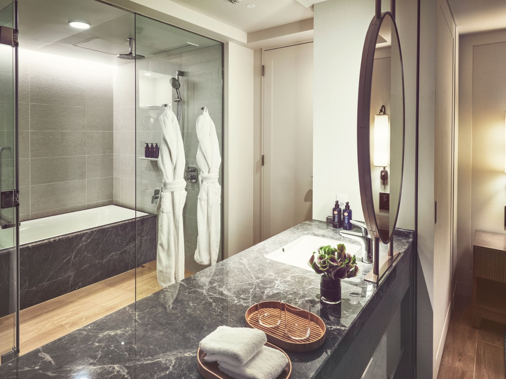 A modern bathroom with a glass shower enclosure, a marble countertop, a sink, and a mirror.
