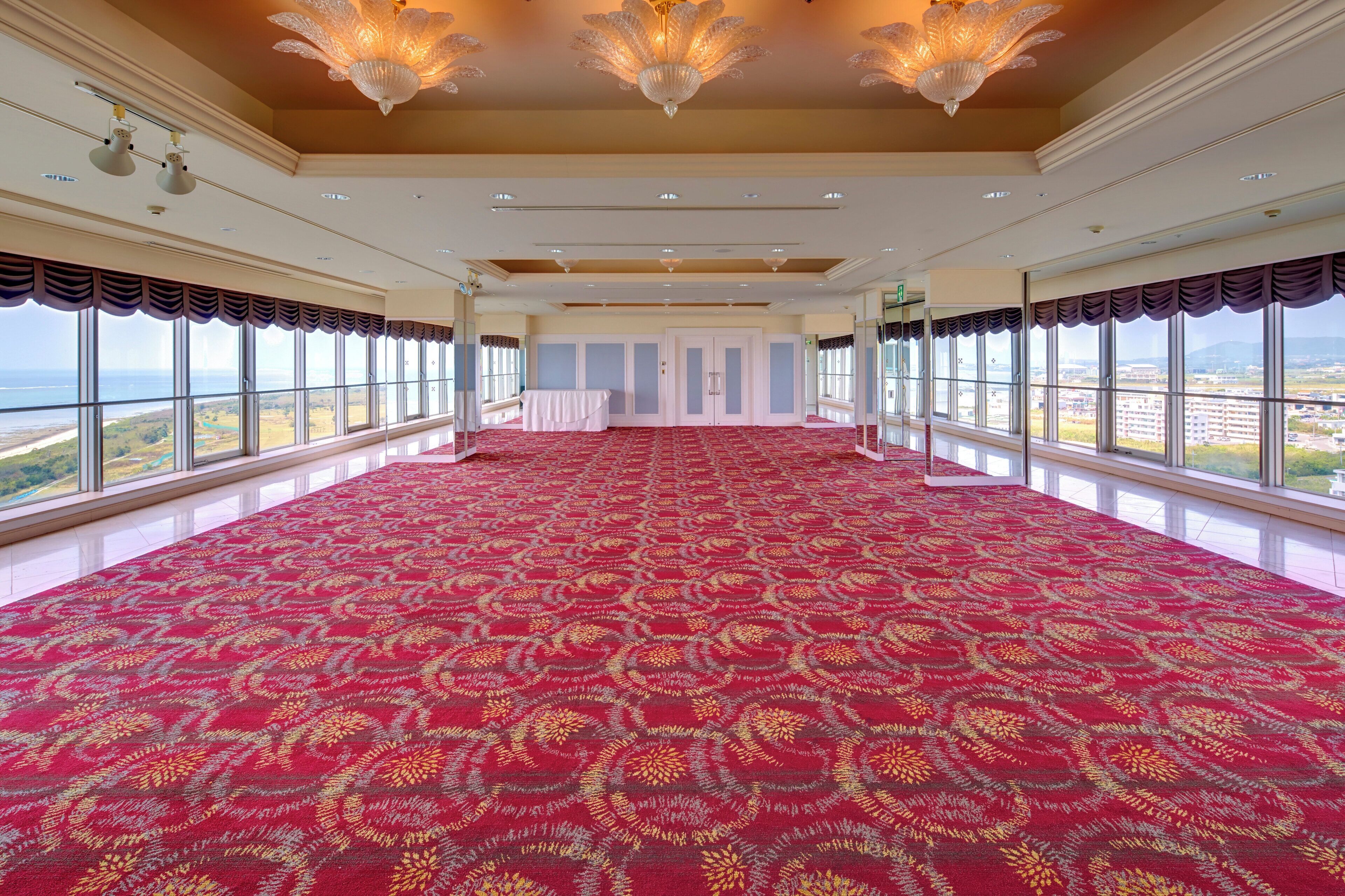 Une pièce spacieuse avec un tapis rouge à motifs, de grandes fenêtres donnant sur un beau paysage et un lustre.