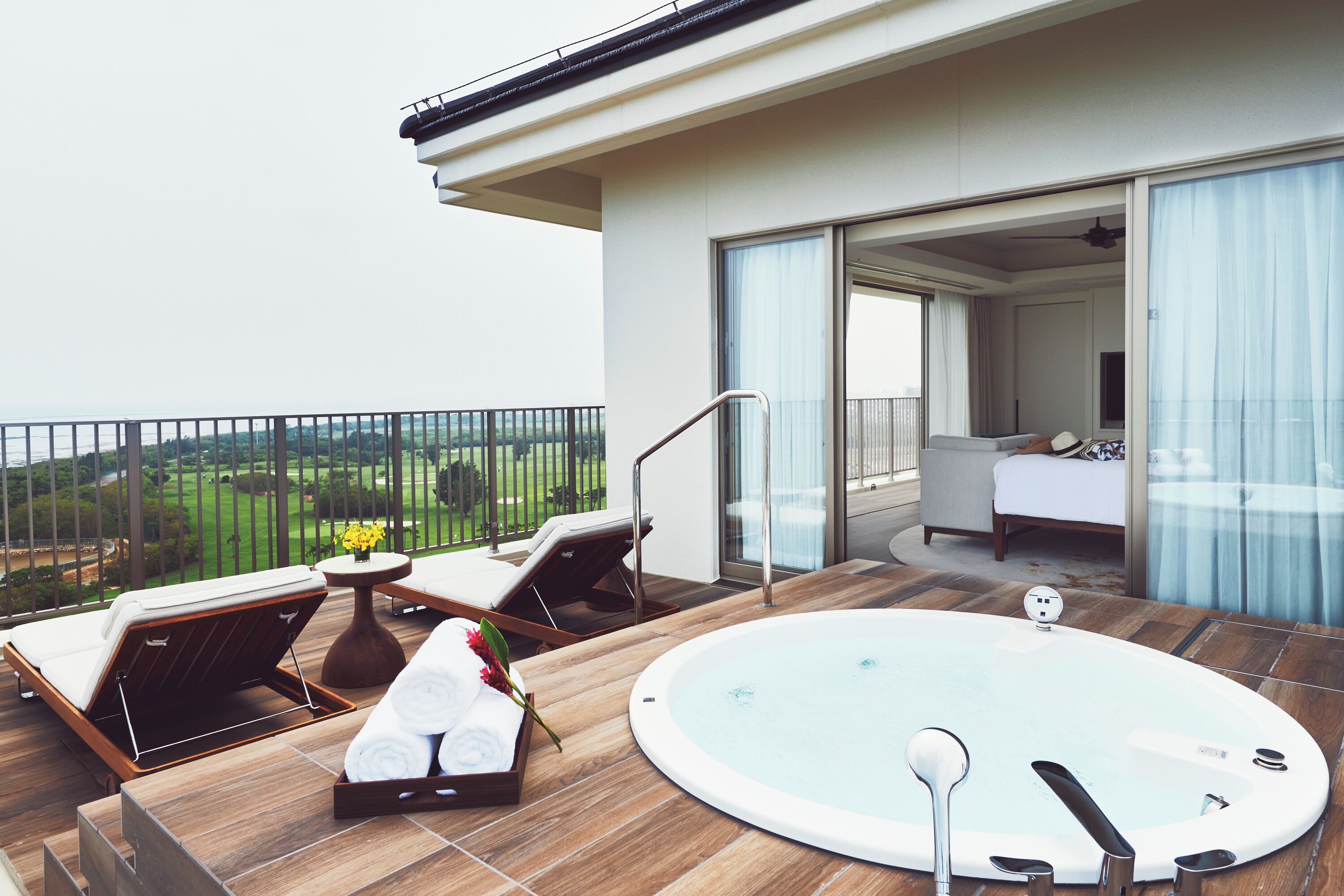 A modern balcony with a hot tub, lounge chairs, and a view of the countryside.