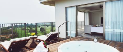 A modern balcony with a hot tub, lounge chairs, and a view of the countryside.