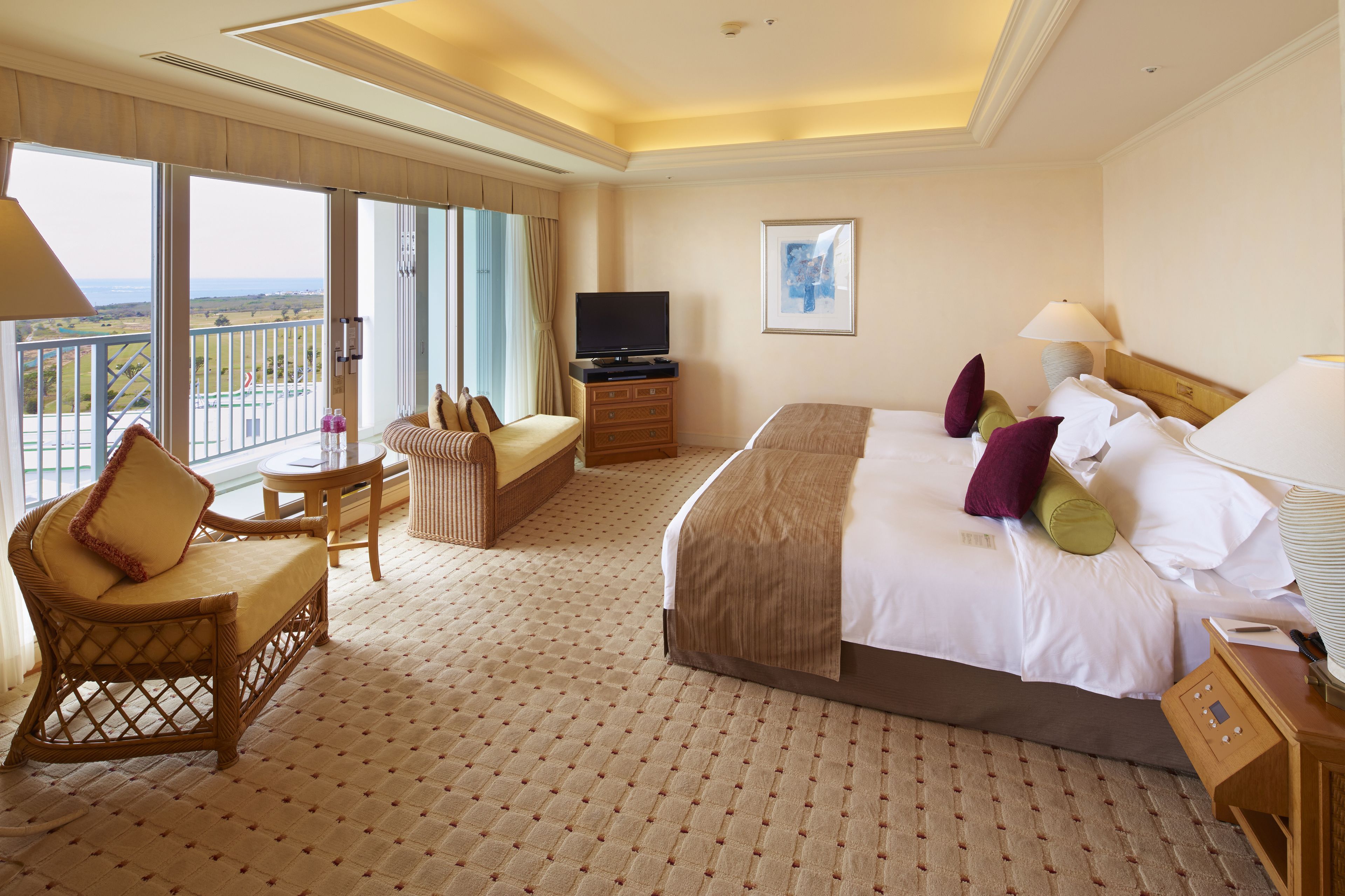 Habitación de hotel con una cama grande, un sofá, una televisión y un balcón con vistas.