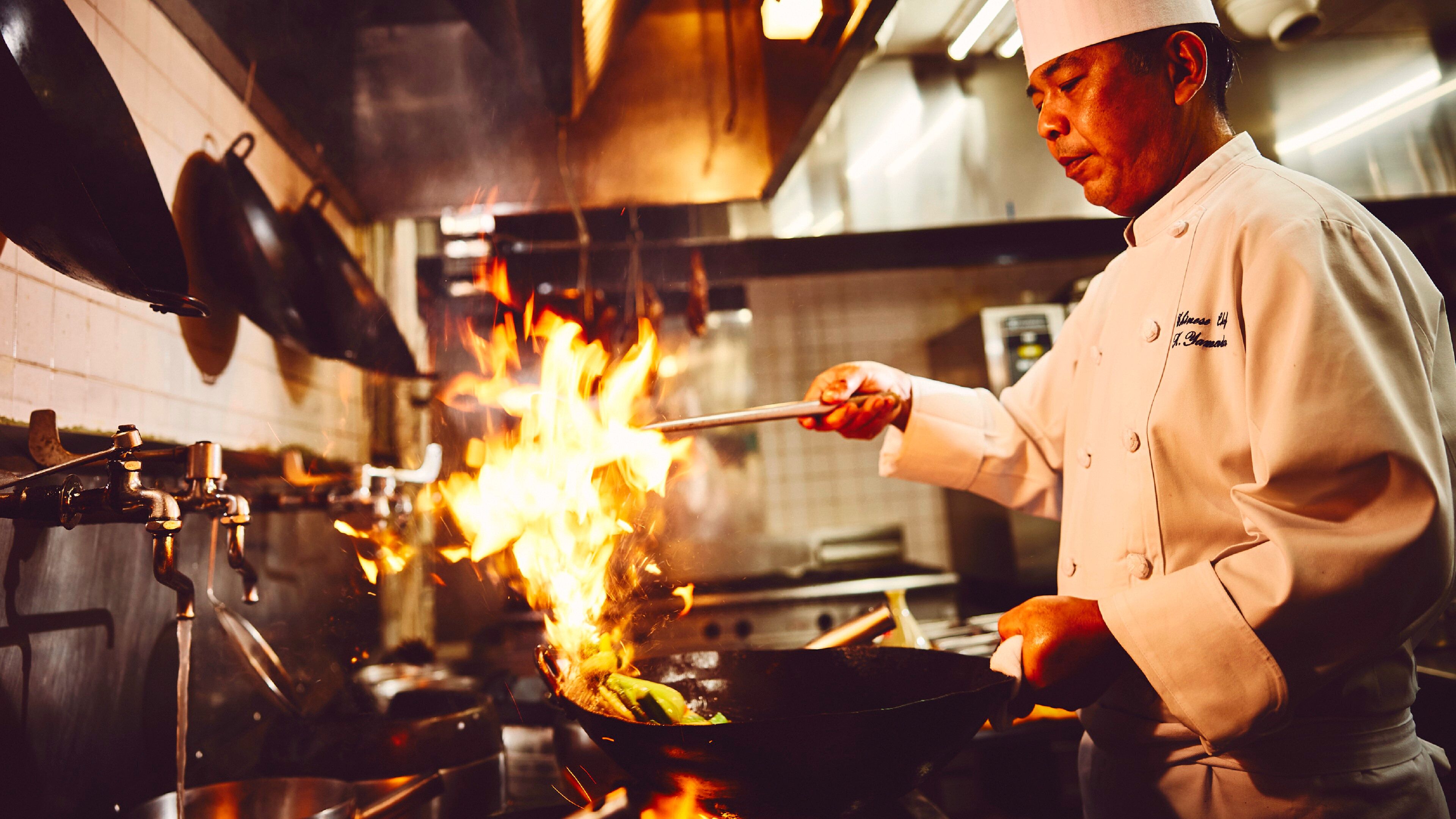 A chef cooking with a large flame in a professional kitchen.