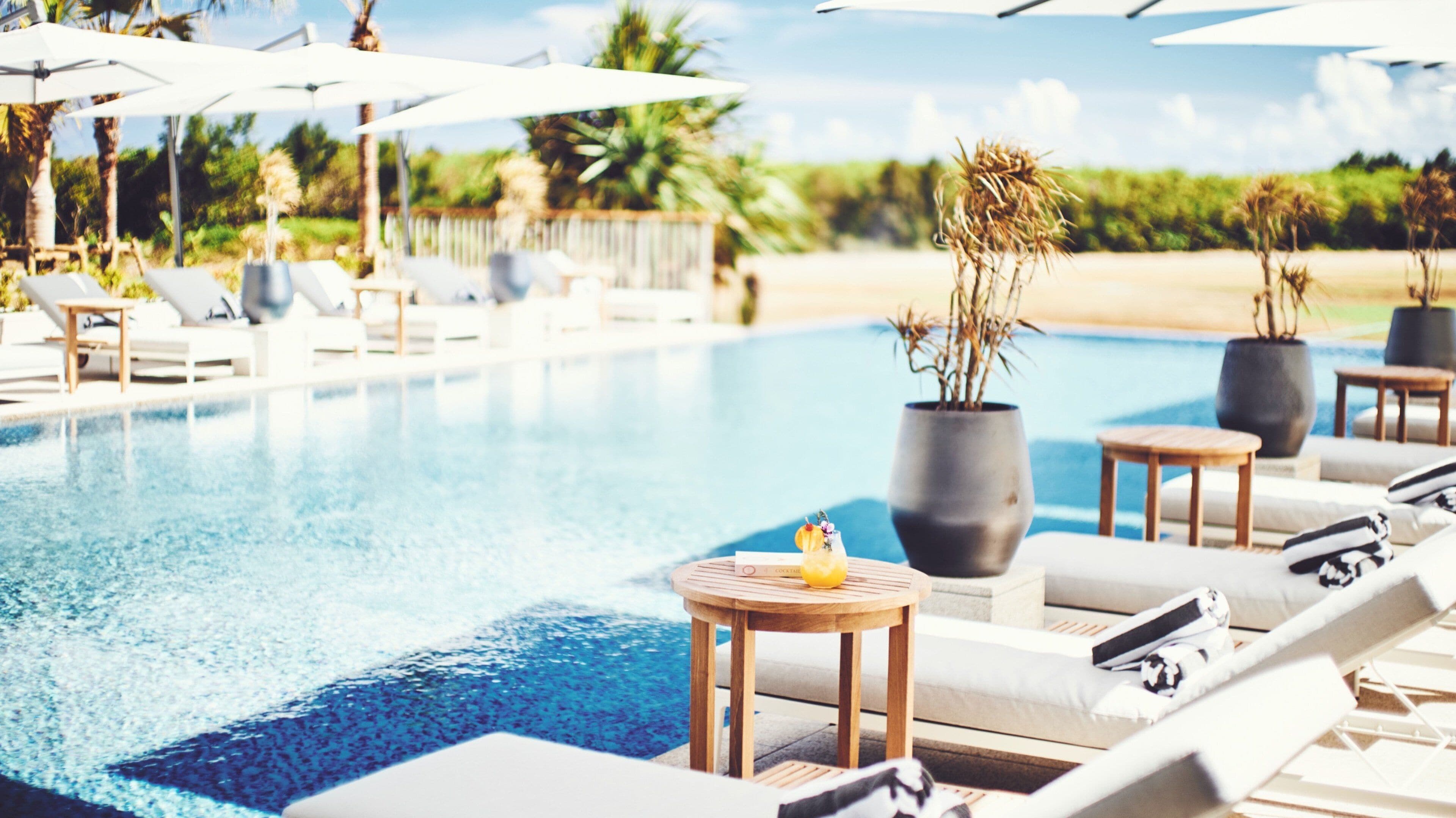 A poolside area with lounge chairs, umbrellas, and a small table with a drink.