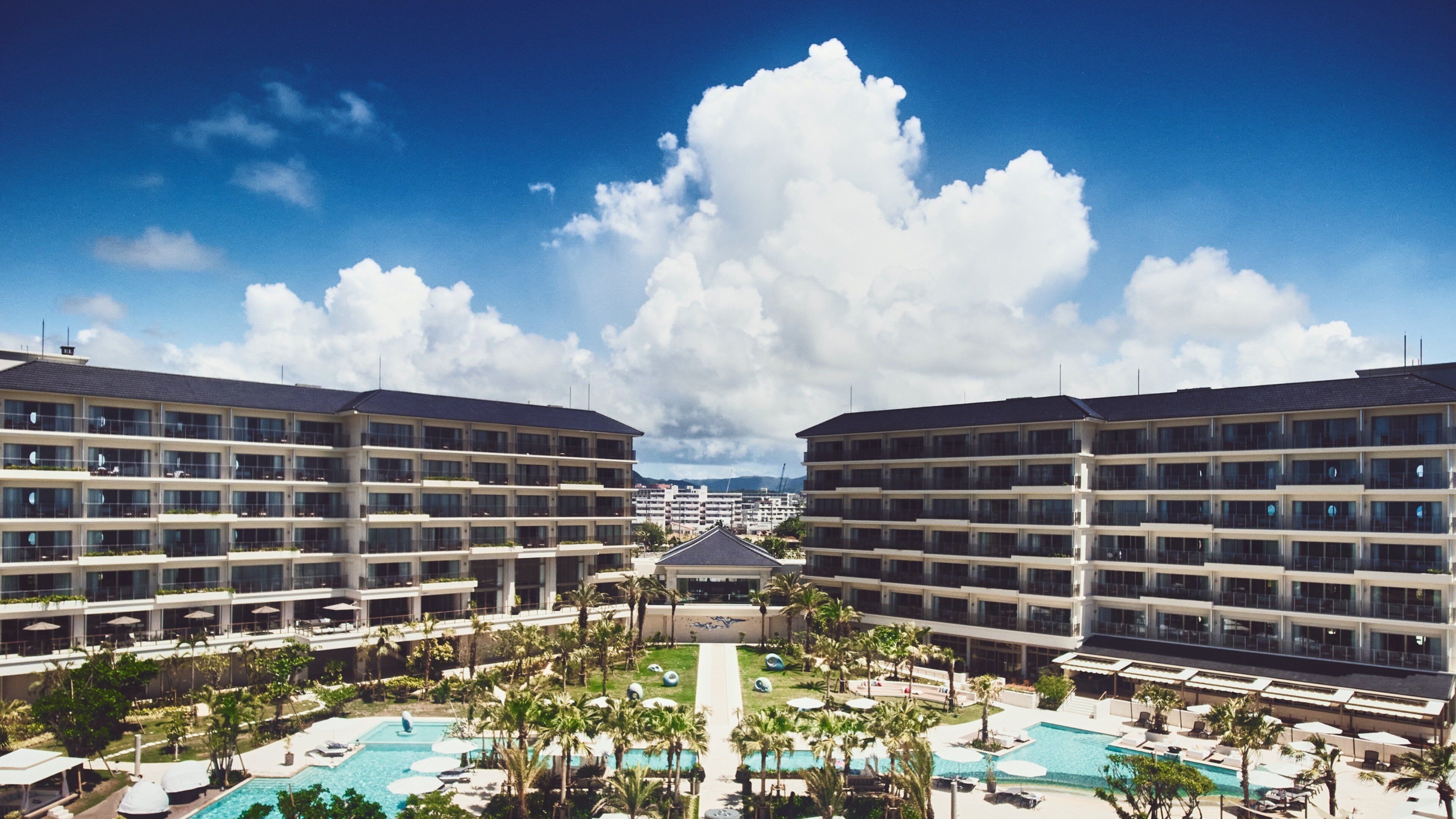 A hotel with multiple floors, a central pool area, and a clear sky.