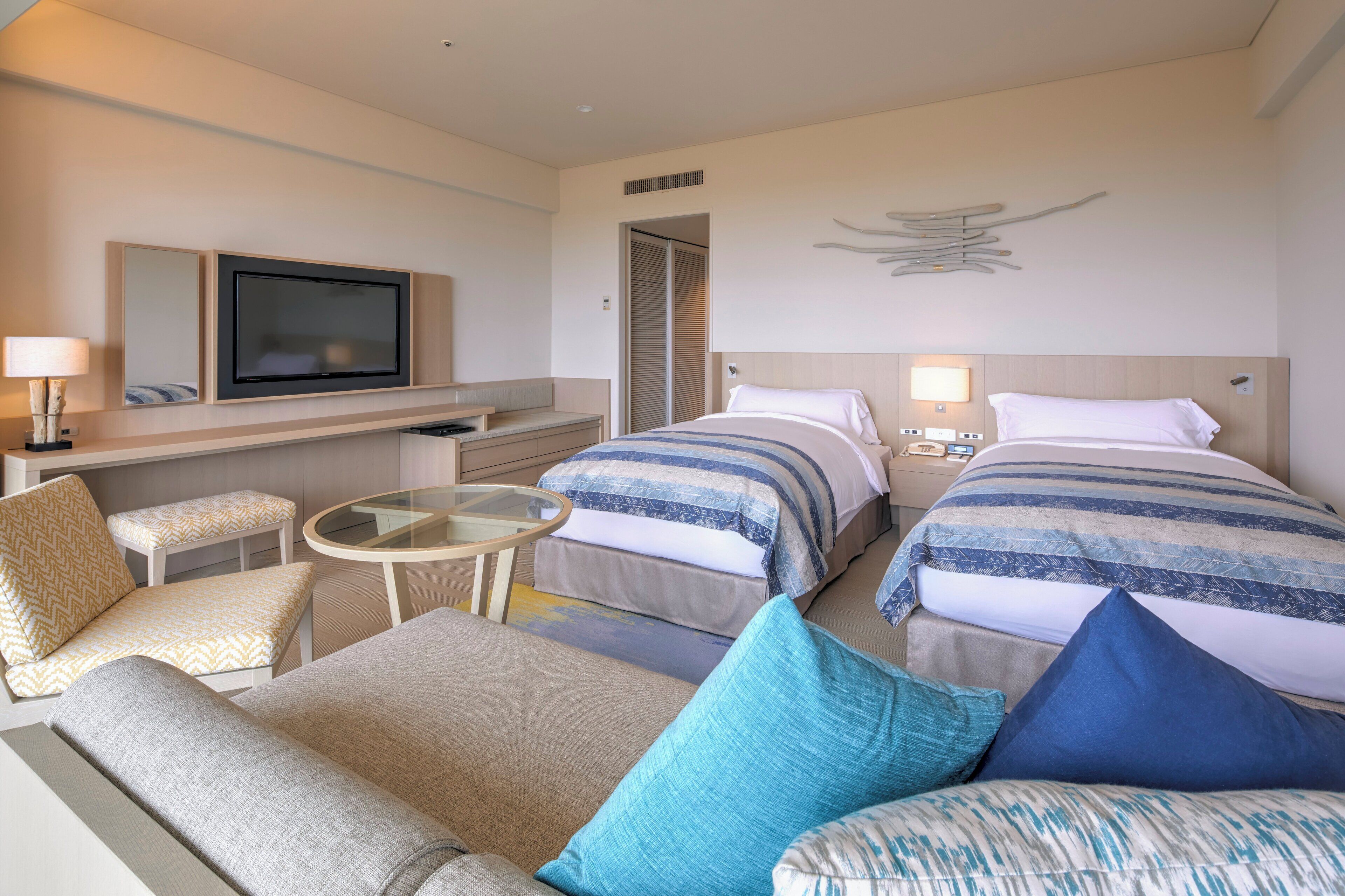 A hotel room with two beds, a sofa, a small table, a TV, and a mirror.