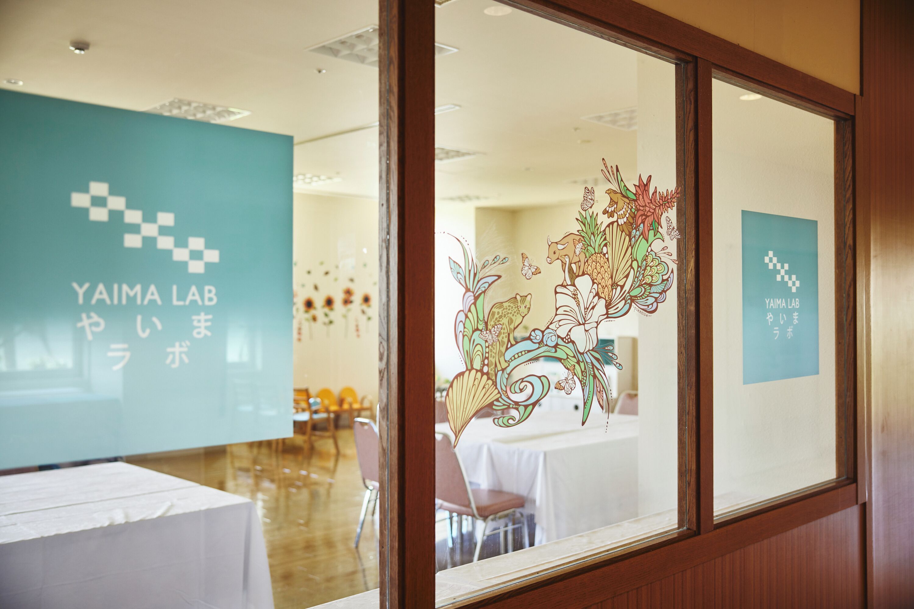 A conference room with a table covered in a white tablecloth, a wooden-framed window, and a decorative glass panel with a floral design.
