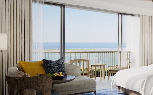 Ein Hotelzimmer mit Balkon und Meerblick, ein Bett, eine Couch mit Kissen, ein kleiner Tisch mit Lampe und ein Sessel.