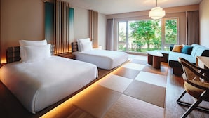A hotel room with two beds, a sofa, a chair, and a view of greenery outside.