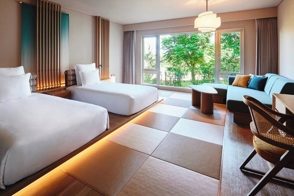 Une chambre d’hôtel avec deux lits, un canapé, un fauteuil et une vue sur la verdure.
