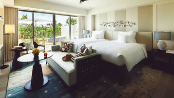 Quarto de hotel com uma cama grande, um sofá, uma mesinha com um vaso de flores e vista para o exterior.