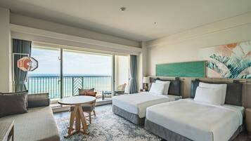 Habitación de hotel con dos camas, un sofá, una mesa de comedor y vista al mar.